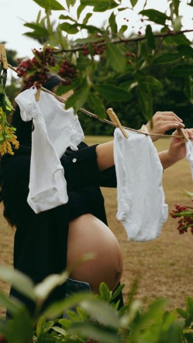 pregnant woman hanging babys laundry in a garden